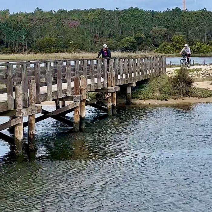 Cyclists crossing a wooden bridge over a coastal lagoon