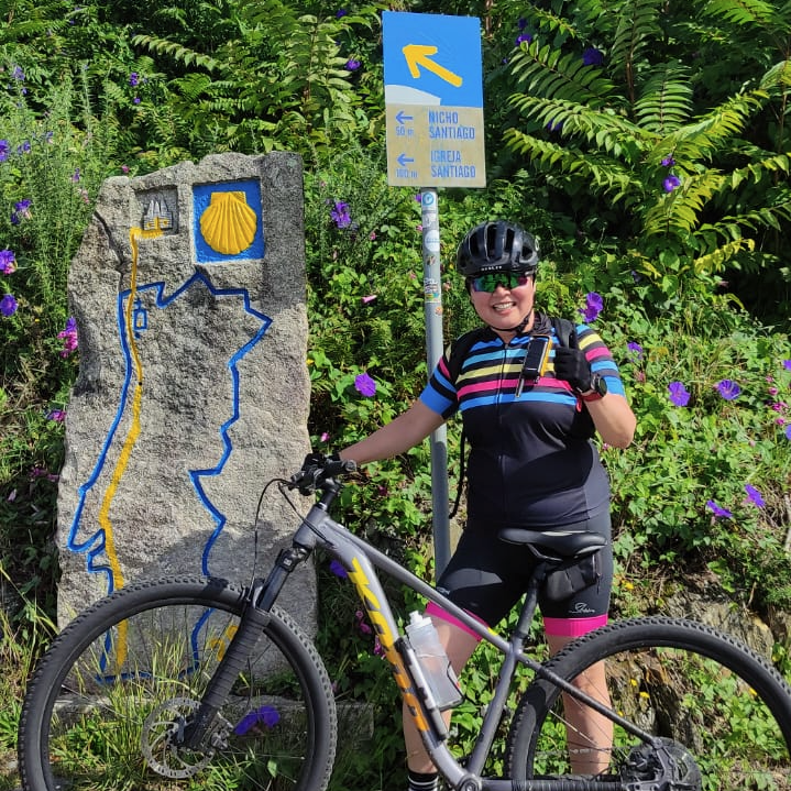 Cyclist beside a Camino waymarker surrounded by green foliage