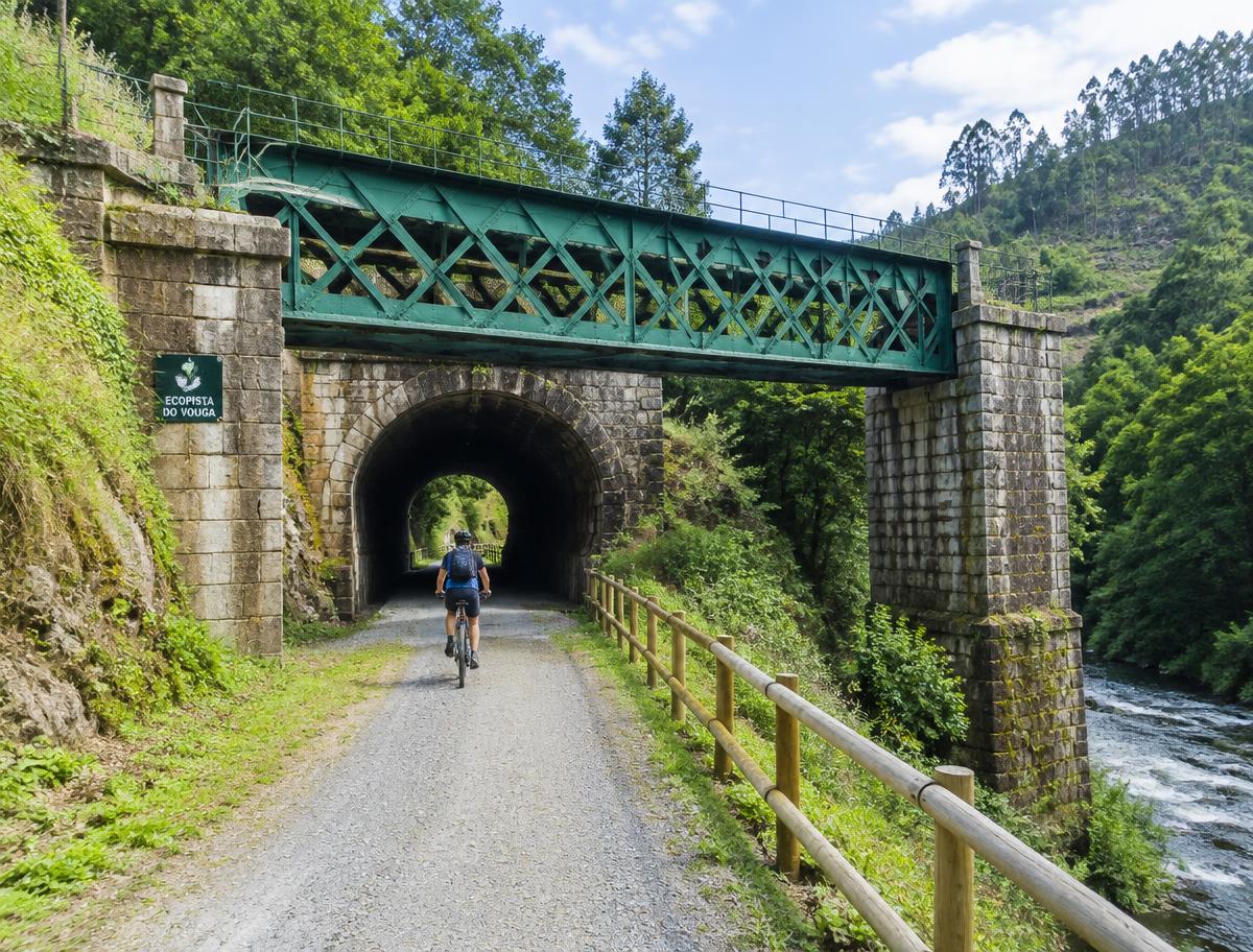 Cyclist entering an old tunnel beneath a green railway bridge on the Vouga greenway